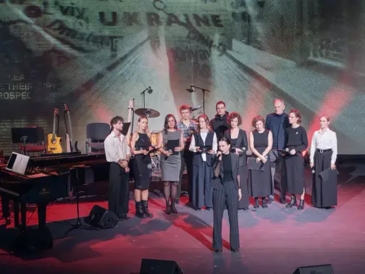 Grupa artystów na scenie, gdzie odbywa się koncert dla Ukrainy. W tle ekran z napisem "UKRAINE".