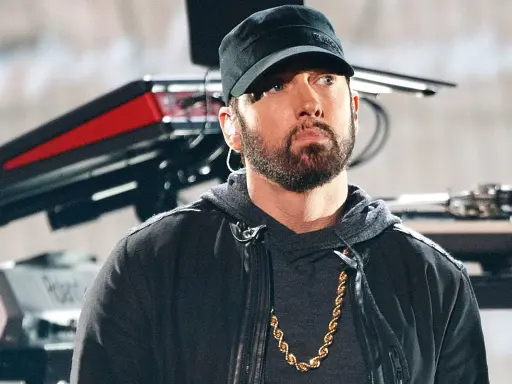 Eminem w czapce i z łańcuchem na szyi. W tle sprzęt muzyczny. Ciekawe, ile ma lat Eminem?