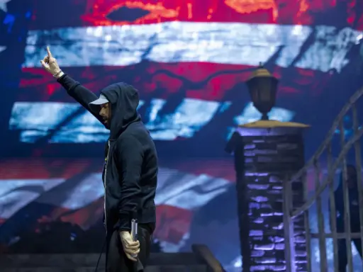 Eminem na koncercie, z palcem w górze, na tle amerykańskiej flagi. Czy Eminem nie lubi Polaków? Nie ma dowodów na to w jego twórczości.