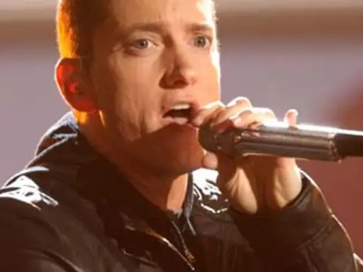 Eminem śpiewa do mikrofonu. Choć jego wzrost, czyli ile Eminem ma wzrostu, nie jest widoczny, jego energia na scenie jest ogromna.