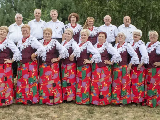 Grupa ludzi w strojach ludowych, kobiety w czerwonych korale i wzorzystych spódnicach, mężczyźni w białych koszulach. Kto śpiewa czerwona jarzębina?