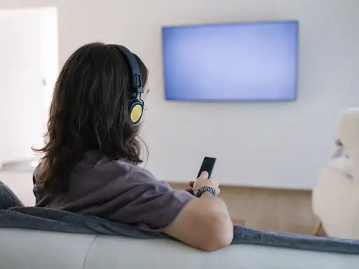 Osoba w słuchawkach z pilotem w ręku, szuka sposobu, jak podłączyć słuchawki bezprzewodowe do telewizora bez bluetooth.