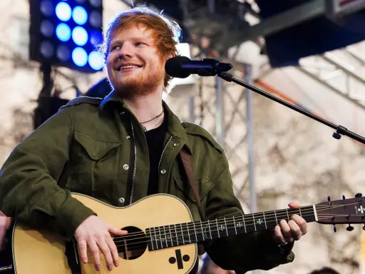 Ed Sheeran uśmiecha się, grając na gitarze akustycznej Martin.