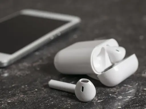 Białe słuchawki bezprzewodowe i smartfon na ciemnym tle. Jedna słuchawka leży obok etui, zastanawiasz się, dlaczego działa tylko jedna słuchawka bezprzewodowa?