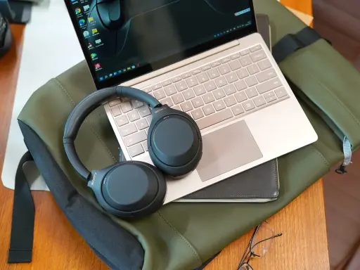 Słuchawki bezprzewodowe Sony leżą na laptopie i zielonej torbie.