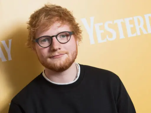 Ed Sheeran w okularach i czarnej bluzie, na tle napisu "YESTERDAY". Wygląda jakby zastanawiał się, kiedy urodził się Ed Sheeran.