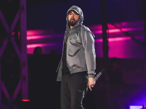 Eminem na scenie w szarej bluzie z kapturem i czarnych spodniach, trzymający mikrofon.