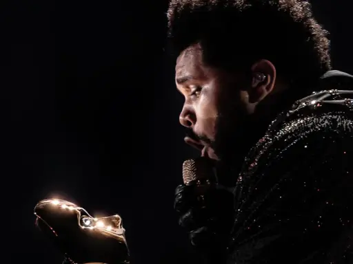 The Weeknd w błyszczącej kurtce, z mikrofonem w dłoni, zastanawia się, ile trwa koncert The Weeknd.