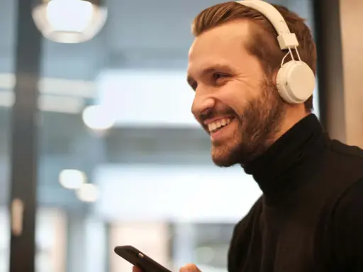 Uśmiechnięty mężczyzna w białych słuchawkach na uszach trzyma smartfon.
