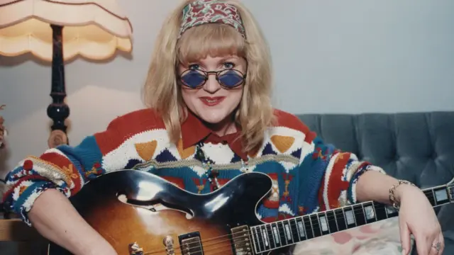 Kto śpiewa mydelko fa? Kobieta z gitarą, w kolorowym swetrze i okularach, gotowa do rock'n'rolla.