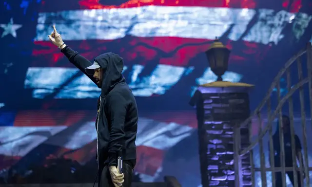 Eminem na koncercie, z palcem w górze, na tle amerykańskiej flagi. Czy Eminem nie lubi Polaków? Nie ma dowodów na to w jego twórczości.