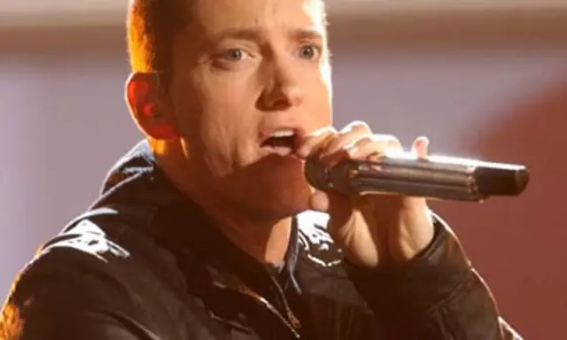 Eminem śpiewa do mikrofonu. Choć jego wzrost, czyli ile Eminem ma wzrostu, nie jest widoczny, jego energia na scenie jest ogromna.