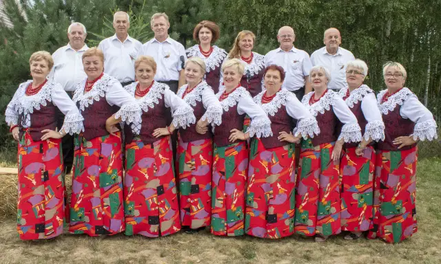 Grupa ludzi w strojach ludowych, kobiety w czerwonych korale i wzorzystych spódnicach, mężczyźni w białych koszulach. Kto śpiewa czerwona jarzębina?