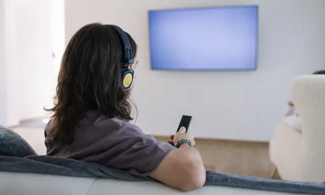 Osoba w słuchawkach z pilotem w ręku, szuka sposobu, jak podłączyć słuchawki bezprzewodowe do telewizora bez bluetooth.