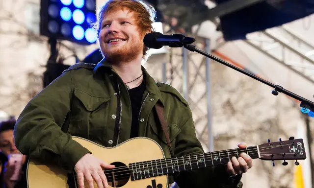 Ed Sheeran uśmiecha się, grając na gitarze akustycznej Martin.