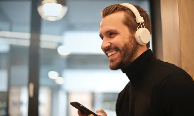 Uśmiechnięty mężczyzna w słuchawkach na uszach trzyma telefon. Proste jak podłączyć słuchawki przewodowe do telefonu Samsung.