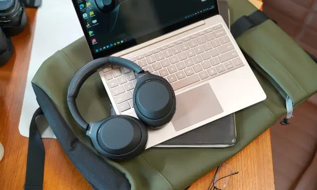 Słuchawki bezprzewodowe Sony leżą na laptopie i zielonej torbie.