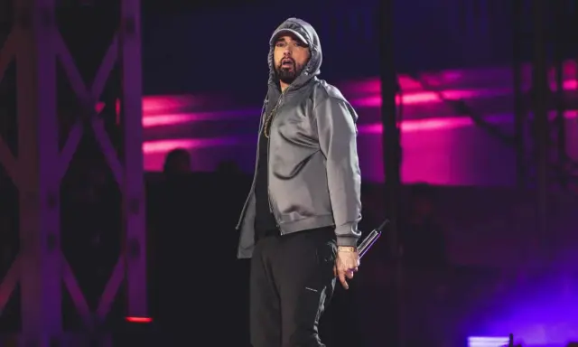 Eminem na scenie w szarej bluzie z kapturem i czarnych spodniach, trzymający mikrofon.
