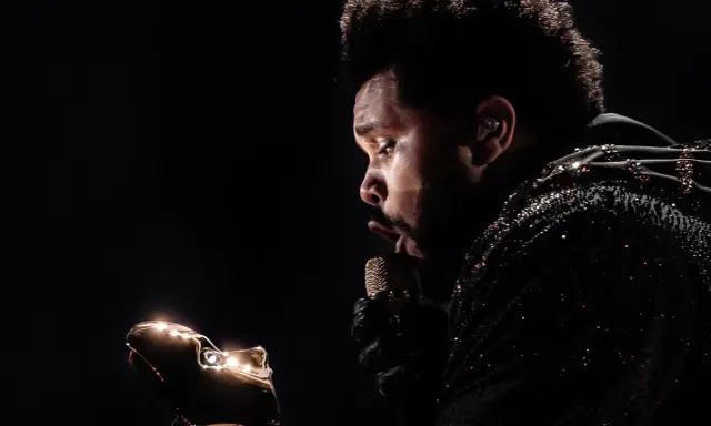 The Weeknd w błyszczącej kurtce, z mikrofonem w dłoni, zastanawia się, ile trwa koncert The Weeknd.