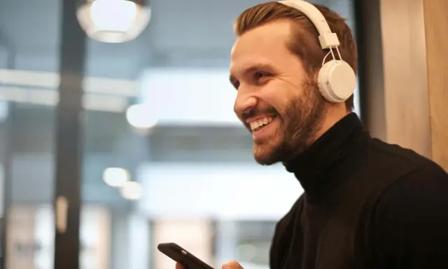 Uśmiechnięty mężczyzna w białych słuchawkach na uszach trzyma smartfon.