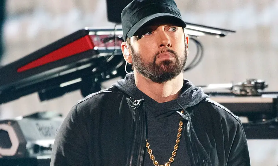 Eminem w czapce i z łańcuchem na szyi. W tle sprzęt muzyczny. Ciekawe, ile ma lat Eminem?