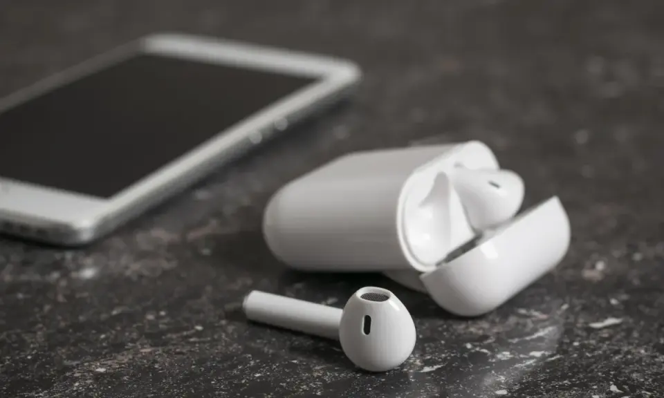 Białe słuchawki bezprzewodowe i smartfon na ciemnym tle. Jedna słuchawka leży obok etui, zastanawiasz się, dlaczego działa tylko jedna słuchawka bezprzewodowa?