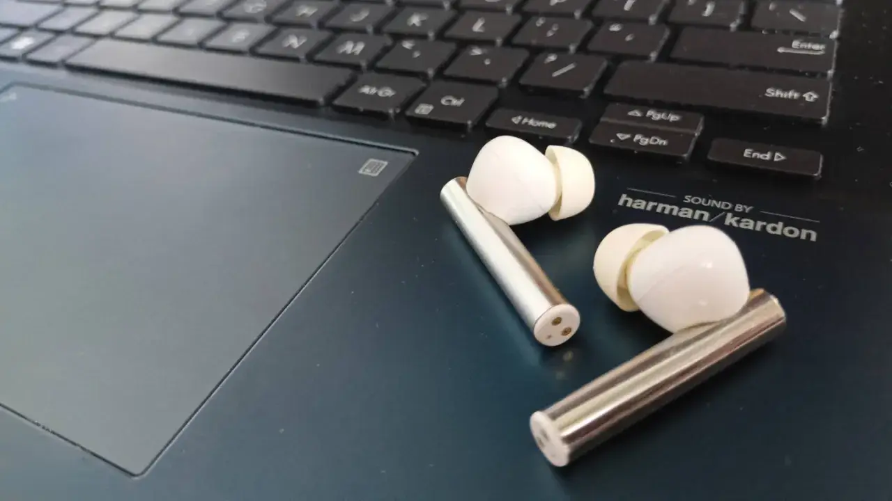 Białe słuchawki bezprzewodowe leżą obok klawiatury laptopa. Dowiedz się, jak sparować słuchawki z urządzeniem.