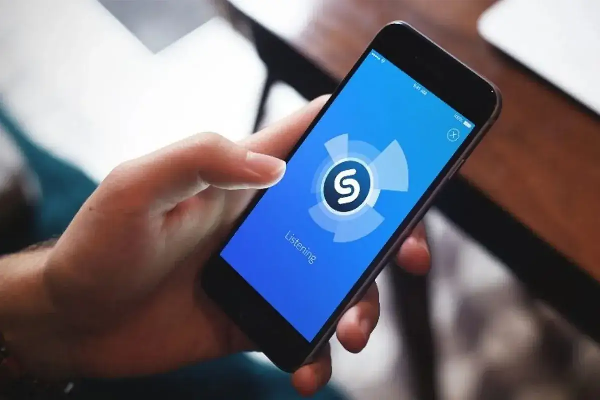 Dłoń trzyma smartfon z aplikacją Shazam, która nasłuchuje, kto śpiewa tą piosenkę.