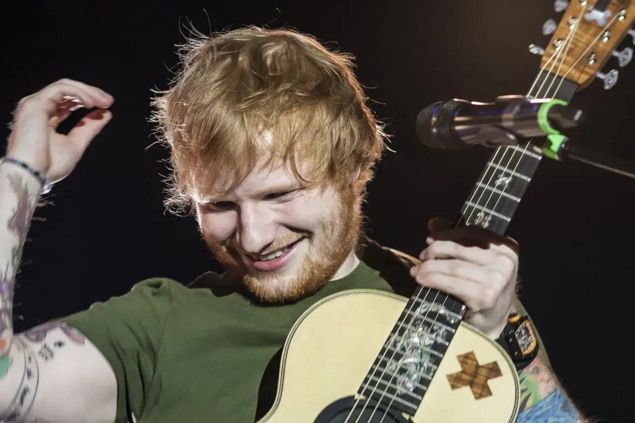 Ed Sheeran uśmiecha się, grając na gitarze. Zastanawiasz się, ile trwa koncert Eda Sheerana?