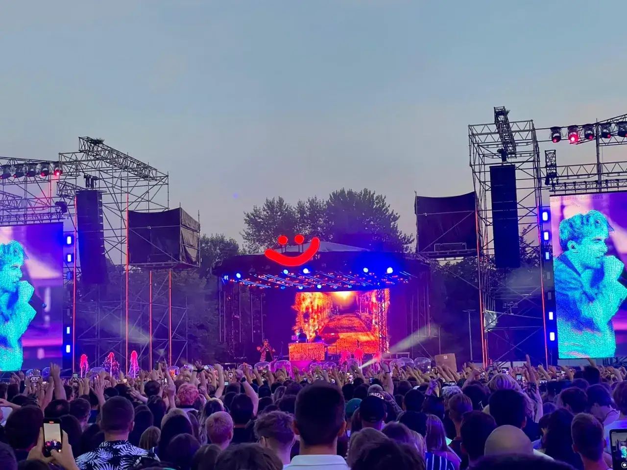 Tłum na koncercie Maty, z wielkimi ekranami po bokach i uśmiechniętą buźką nad sceną. Fani bawią się, nie wiedząc, ile trwają koncerty Maty.