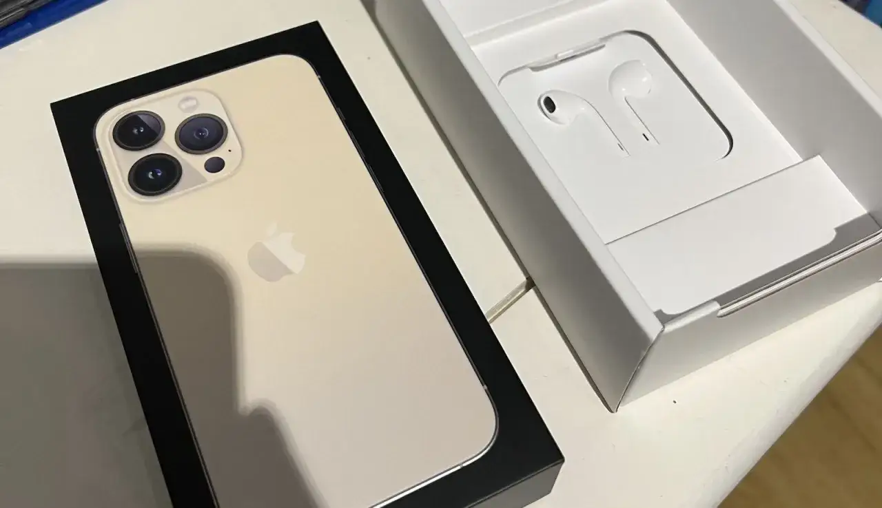 Złoty iPhone 13 Pro w pudełku obok słuchawek. Idealny zestaw, jeśli zastanawiasz się, jakie słuchawki do iPhone 13.
