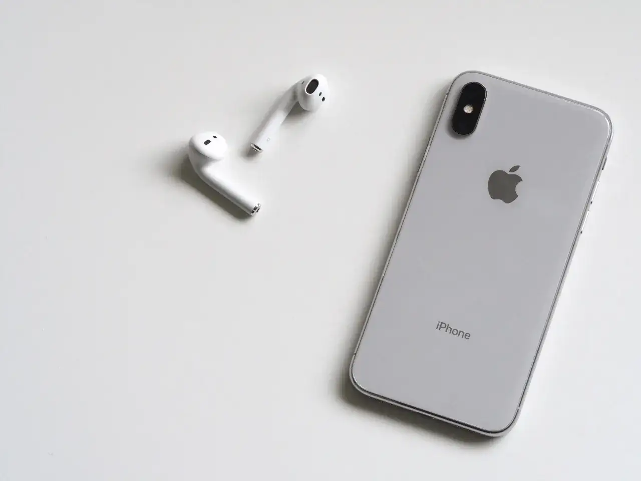 Srebrny iPhone i białe słuchawki AirPods. Idealny zestaw, jeśli zastanawiasz się, jakie słuchawki do iPhone 13.
