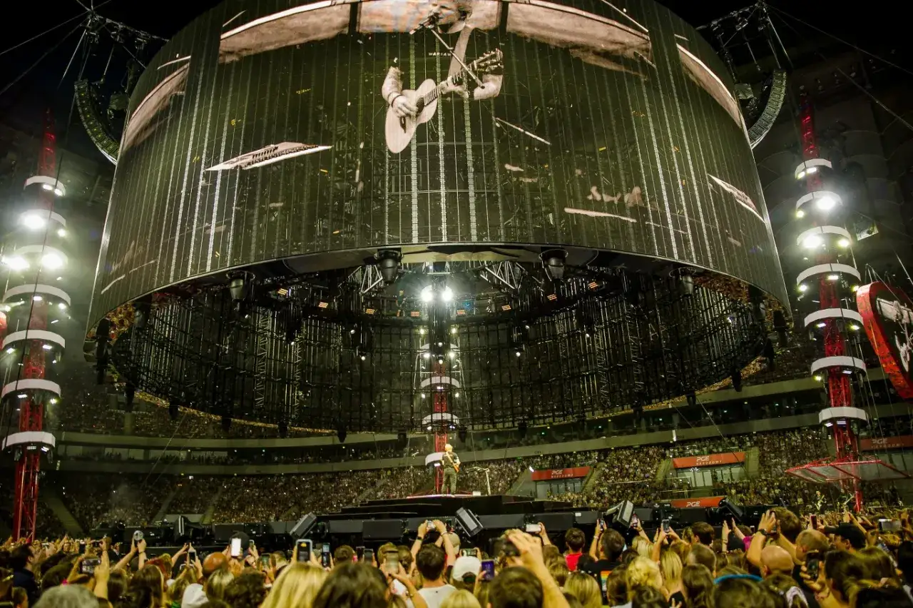 Ed Sheeran w Warszawie zgromadził tłumy. Ogromny ekran pokazuje artystę, a pod nim tysiące fanów z telefonami.