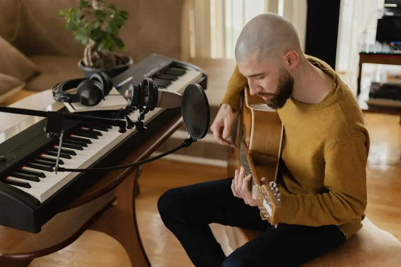 Mężczyzna gra na gitarze przy pianinie i mikrofonie. Tworzy muzykę, kt&oacute;ra pomoże mu sprzedać tekst piosenki.