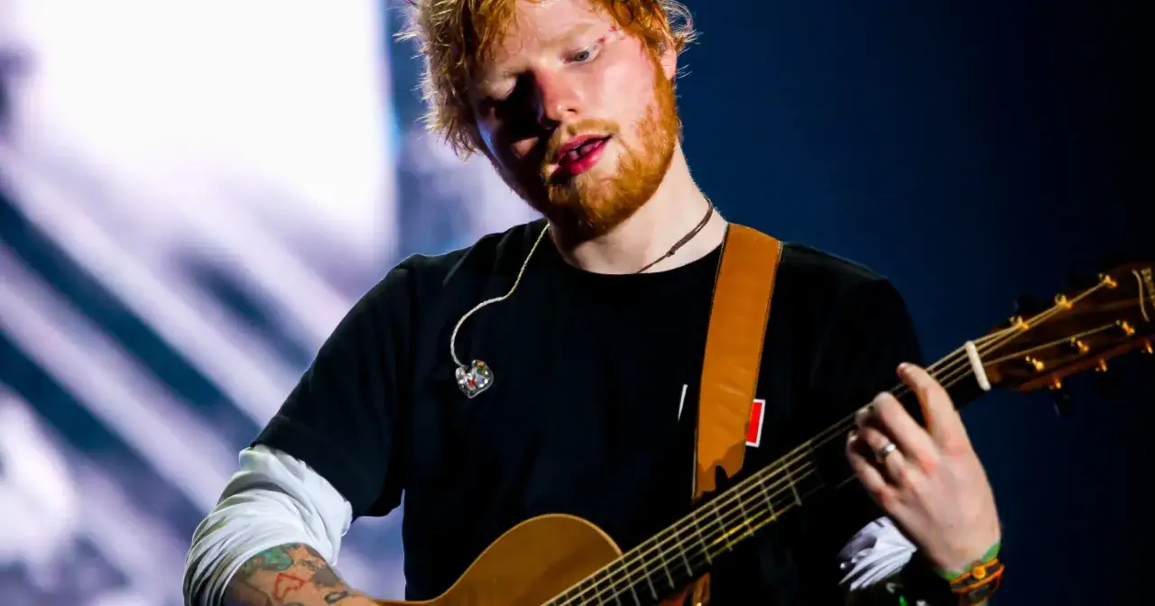 Ed Sheeran, grający na gitarze, z charakterystyczną rudą brodą i włosami. Warto wiedzieć, ile lat ma Ed Sheeran, by docenić jego karierę.
