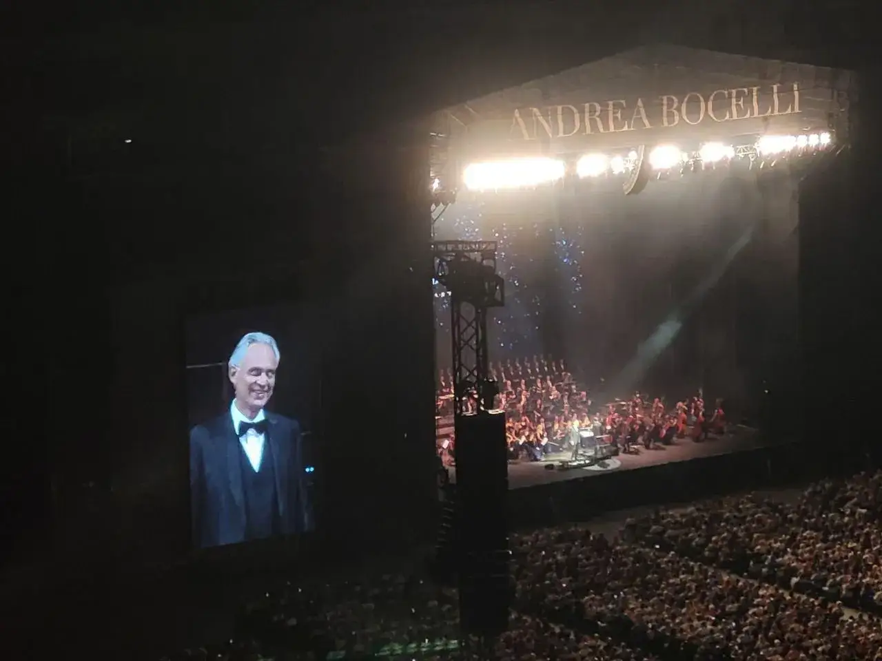 Koncert Andrei Bocellego w Warszawie. Na ekranie jego uśmiechnięta twarz, na scenie orkiestra i ch&oacute;r.