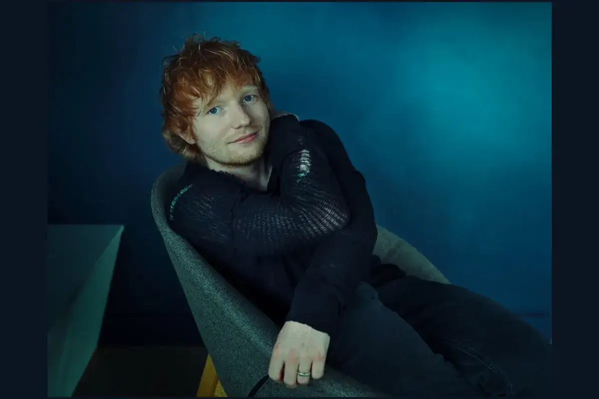 Ed Sheeran, z rudymi włosami i niebieskimi oczami, siedzi w fotelu. Czy Ed Sheeran grał w Harrym Potterze? Nie, ale jego uśmiech m&oacute;głby rozjaśnić Hogwart.