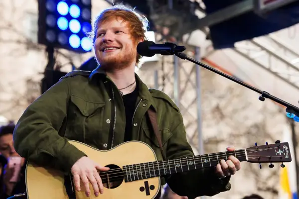 Ed Sheeran uśmiecha się, grając na gitarze akustycznej Martin.